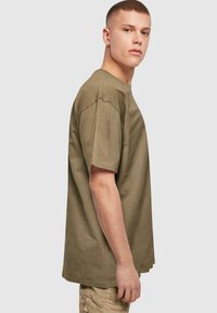 Olivengrøn bomulds t-shirt med løs pasform, korte ærmer og rund halsudskæring, der viser tekstureret stof og minimalistiske syninger.