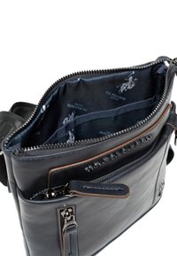 Borsa a tracolla in pelle nera con due scomparti con zip, foderata in tessuto blu contrassegnato da loghi e testo bianchi all'interno di uno scomparto.