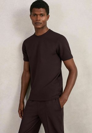 Tricou scurt cu mâneci, de culoare maro închis, realizat dintr-un material de bumbac neted, având un gât clasic și o croială lejeră, asortat cu pantaloni în aceeași nuanță.