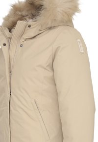 Giacca puffer beige con cappuccio bordato in pelliccia, chiusura a zip, tasche laterali e un tessuto testurizzato. Presenta un piccolo logo sulla manica.
