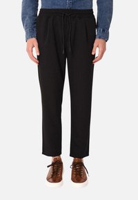 Pantaloni neri a sigaretta con cintura elastica e lacci, abbinati a sneakers marroni con lacci. Tessuto liscio e morbido, design minimalista.