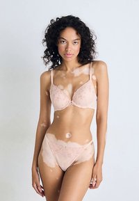 Súprava svetloružovej čipkovanej spodnej bielizne, ktorá obsahuje podprsenku s vypchávkami a nastaviteľnými ramienkami a zodpovedajúce bikinové nohavičky, oboje s kvetinovým vzorom.