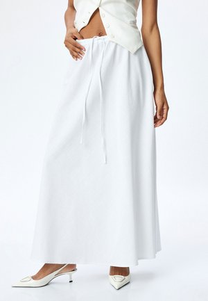 Jupe maxi blanche avec taille à cordon, en tissu léger, silhouette en A, présentant un motif texturé, assortie à des talons slingback blancs.