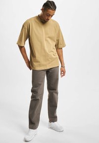 Tricou din bumbac bej deschis, cu un croi lejer și mâneci scurte, asortat cu pantaloni gri largi și adidași albi. Design simplu, fără modele.