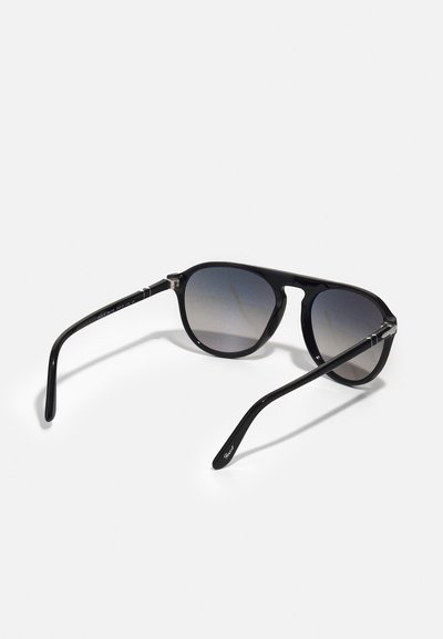 Óculos de sol pretos com um design arredondado, lentes graduadas e um acabamento brilhante. Hastes finas pretas com detalhes em prata na dobradiça.