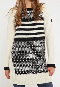 Sweter dziewiarski z czarno-białymi paskami w górnej części, wzorzystą dolną częścią oraz ściągaczami przy mankietach i dolnym końcu. Przyjemny, teksturowany materiał.