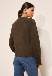 Brūns adīts džemperis ar apaļu kakla izgriezumu un ribotu apakšmalu. Apvienots ar ziliem džinsiem, kuriem ir vienkāršs, teksturēts dizains.