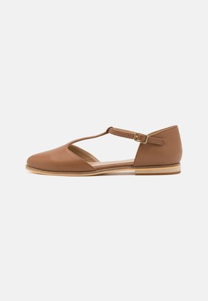 Chaussure plate en cuir brun avec un design à découpes, une bride de cheville et une semelle en bois clair. Présente un bout arrondi et une texture lisse.