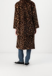 Nepbontjas met luipaardprint, voorzien van een kraag, lange mouwen en een rechte snit. Draagt over lichtblauwe spijkerbroeken en zwarte sneakers.