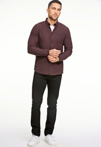 Tumman viininpunainen napitettava paita, jossa on rintatasku, pitkät hihat ja hieman teksturoitu kangas, yhdistettynä mustiin housuihin ja valkoisiin tennareihin.