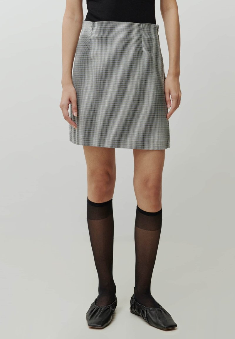 Grijze geruite mini-jurk met een slim fit, platte voorzakken, en gecombineerd met zwarte kniehoge kousen en zwarte platte schoenen.