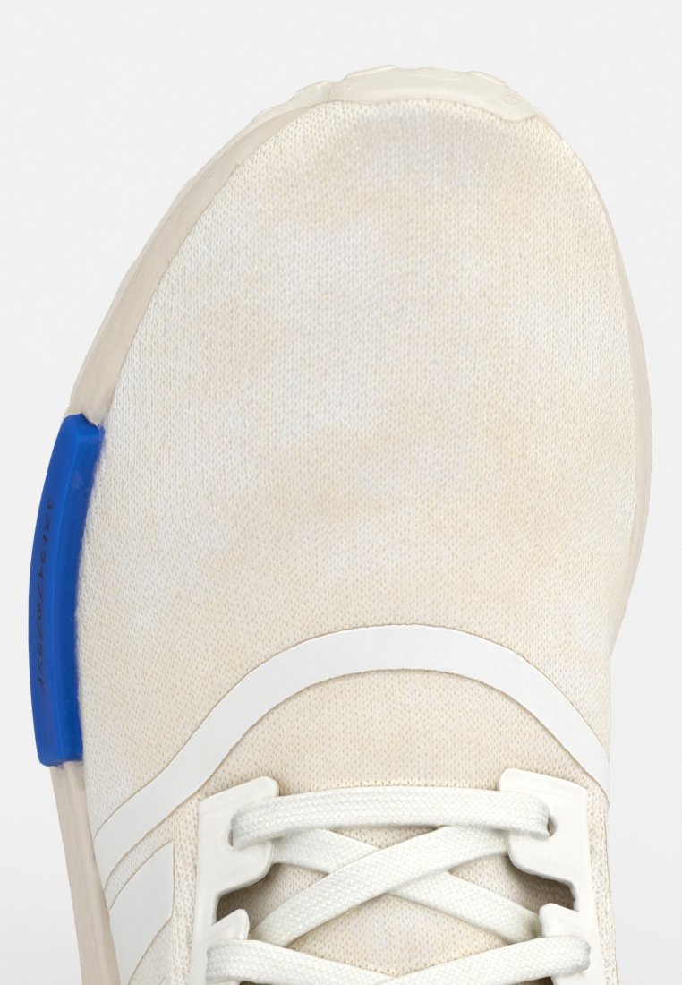 Helle beige Sportschuh mit einer strukturierten Stoffoberfläche, weißen Akzenten und einer blauen Fersenschlaufe. Verfügt über ein traditionelles Schnürdesign.
