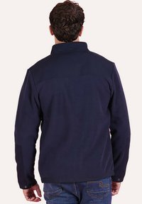 Veste en polaire bleu marine avec un col structuré, des manches longues et un panneau d'épaule contrastant ; texture lisse, poignets boutonnés et coupe décontractée.