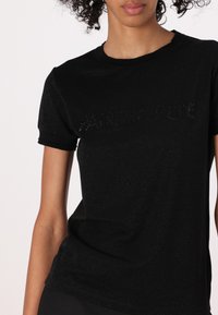 T-shirt nera a maniche corte realizzata in un tessuto lucido, con lettering in rilievo "PATRIZIA PEPE" sul davanti. Design semplice con colletto a girocollo.