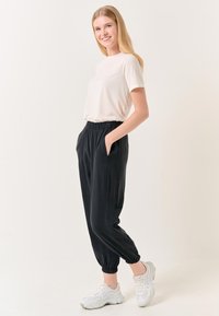 Zwarte joggers met elastische tailleband en zijzakken, gecombineerd met een lichtbeige top met korte mouwen; het model draagt witte sportschoenen.