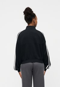 Μαύρο φούτερ με ψηλό γιακά, λευκές ρίγες στο πλάι και ριμπ μανσέτες. Μαλακή υφή και άνετη εφαρμογή, συνδυασμένο με γκρι παντελόνι φόρμας.