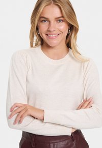 Krémový pletený sveter s okrúhlym výstrihom, rebrovanými manžetami a jemným naberaním na pleciach. Mäkka textúra a priliehavý strih.