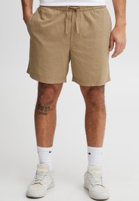 Beige textuur korte broek met een elastische taille en een trekkoord, voorzien van zijzakken en een ontspannen pasvorm. Gecombineerd met witte sokken en sneakers.