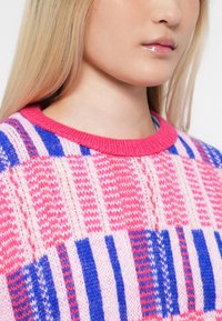 Close-up of a person wearing a pink, blue, and white striped knit sweater with long blonde hair and glossy lips.