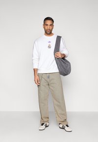 Λευκό φούτερ με μωβ λογότυπο Adidas, ανοιχτό μπεζ τζιν και μαύρα και λευκά αθλητικά παπούτσια· γκρι τσάντα ώμου κρεμασμένη στον έναν ώμο.