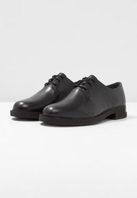 Scarpe nere in pelle con finitura liscia, punta arrotondata, suola piatta in gomma e sistema di allacciatura tradizionale. Accenti di cucitura sottili.