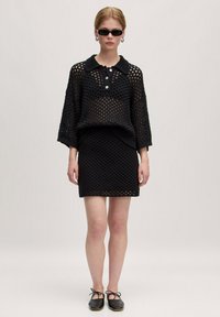Zwart, opengebreid sweater met een kraag, korte mouwen en een drieknoopsluiting, gecombineerd met een bijpassende zwarte minirok.