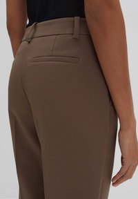 Pantaloni marroni su misura con una texture liscia, dotati di una tasca posteriore piatta e passanti per la cintura, mostrati dalla prospettiva posteriore.