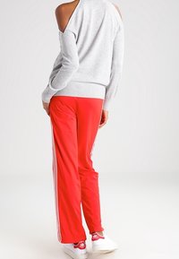 Pull gris à épaules dénudées avec un ourlet côtelé, associé à un pantalon de jogging rouge avec des bandes blanches sur les côtés. Porté avec des baskets blanches.