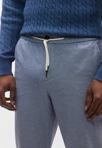 Ανοιχτό μπλε παντελόνι τζόκερ με ελαστική μέση, λευκό κορδόνι και διακριτ ή υφή, συνδυασμένο με πουλόβερ σε σκούρο μπλε με πλεξούδες.