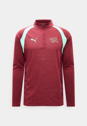 Camiseta deportiva de manga larga color granate con detalles en tono menta claro en los hombros, cremallera parcial, logo de Puma y emblema de la Asociación Suiza de Fútbol en el pecho.