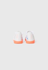Des baskets blanches et orange vues de l'arrière, avec le texte "L'Avenir" et un design graphique bleu sur les côtés.