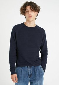 Sudadera texturizada de color azul marino con rayas horizontales, cuello redondo y mangas largas, combinada con pantalones vaqueros de corte holgado.