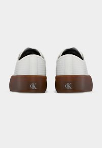 Paire de baskets basses blanches texturées avec semelles épaisses marron et logo cK à l'arrière, vues de dos sur un fond uni.