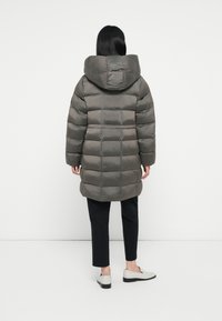 Grijze pufferjas met horizontaal gestikte secties, grote capuchon en een soepele textuur. Draagt over zwarte broeken en grijze schoenen met een lage hak.