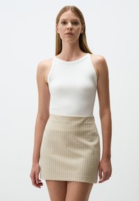 Witte geribde tanktop gecombineerd met een beige minirok met lichte verticale strepen. Zachte texturen en een aansluitend ontwerp.