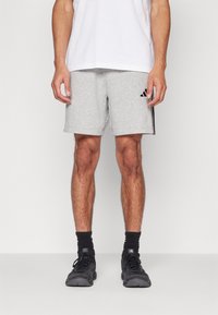 Γκρι αθλητικά σορτς από μείγμα βαμβακιού, με μαύρες ρίγες στο πλάι και κεντημένο λογότυπο στην αριστερή πλευρά. Φοριούνται με λευκό μπλουζάκι.