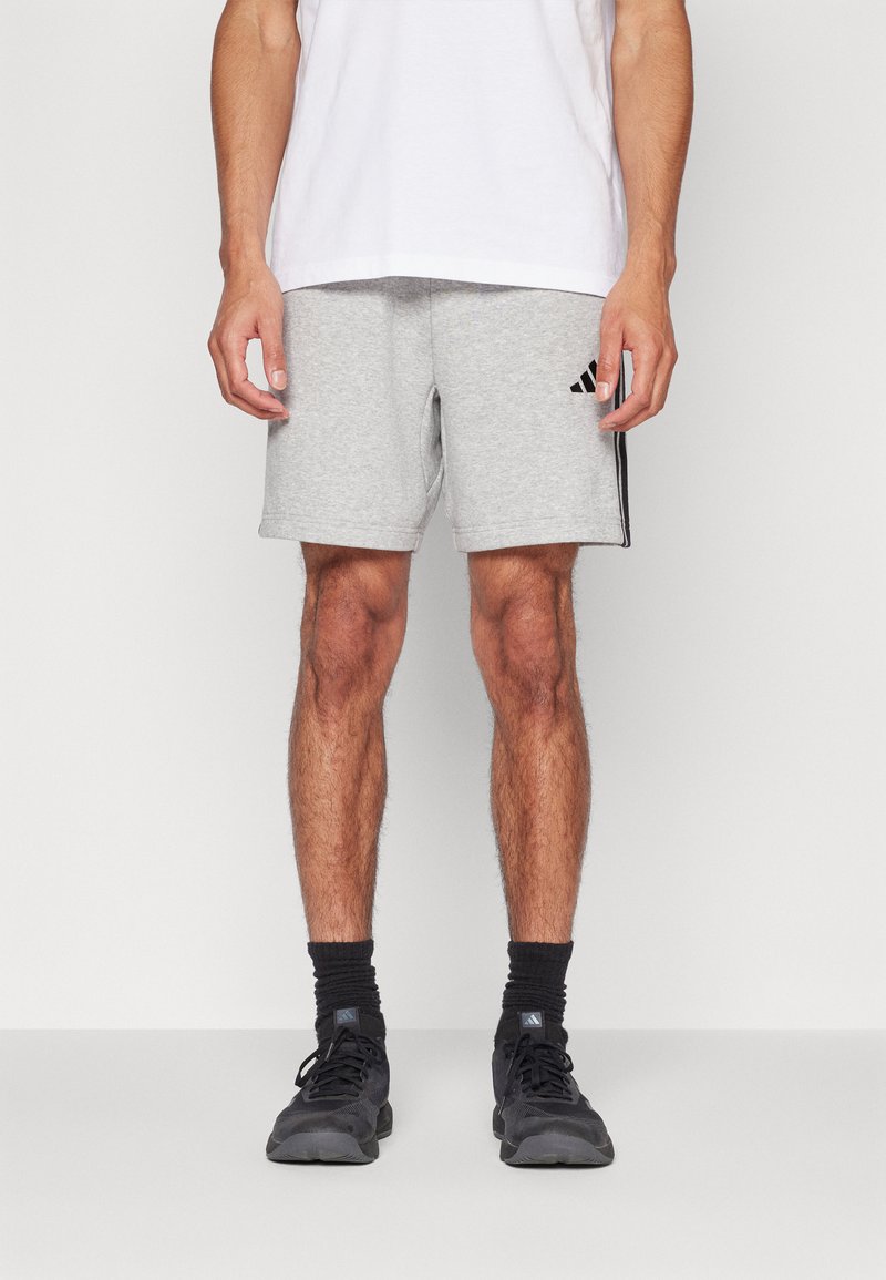 Γκρι αθλητικά σορτς από μείγμα βαμβακιού, με μαύρες ρίγες στο πλάι και κεντημένο λογότυπο στην αριστερή πλευρά. Φοριούνται με λευκό μπλουζάκι.