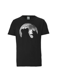 Černé tričko s siluetou postavy s velkýma očima, která drží sušenku, na pozadí bílé měsíční scenérie.
