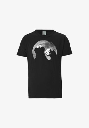 Černé tričko s siluetou postavy s velkýma očima, která drží sušenku, na pozadí bílé měsíční scenérie.