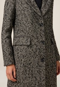 Cappotto in misto lana con motivo a zig zag in nero e crema, modello monopetto con rever a punta e due tasche frontali.