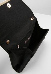 Sac à main en tissu noir avec fermeture à pression dorée et poche intérieure zippée. Texture lisse et grand compartiment ouvert pour le rangement.