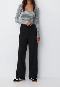 Striped long-sleeve cropped top in green and white, paired with black wide-leg trousers and black sandals with white accents.