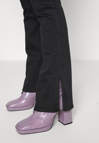 Sapatos de salto plataforma de verniz roxo com bico quadrado e salto bloco, usados com calças de ganga escuras, com flare e fendas laterais.