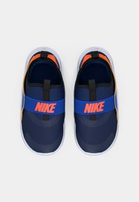 Marine slip-on sko med blå stropp som har "Nike" i oransje, svarte detaljer og teksturert stoff; hvit såle.