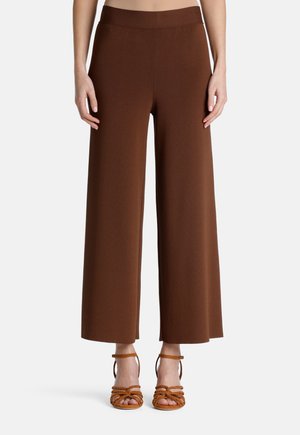 Bruine wijde broek met een gestructureerde stof en een elastische tailleband, aangevuld met tan kleurige sandalen met banden die de tenen laten zien.
