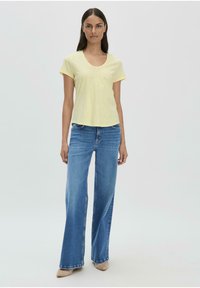 Helles gelbes Kurzarm-T-Shirt mit Rundhalsausschnitt, kombiniert mit weit geschnittenen blauen Jeans und beigen High Heels. Glatte Textur, lässige Passform.