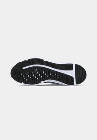 Black and white rubber sole of a sports shoe, showing textured grip pattern and curved tread design.