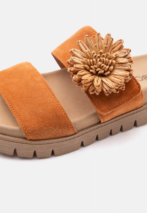 Sandale en daim marron avec deux brides, ornée d'une grande fleur texturée sur la bride supérieure et une semelle épaisse en caoutchouc.