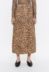 Gonna di denim a stampa leopardata, di lunghezza media, con vita aderente, chiusura anteriore a bottoni e una texture sottile. Abbinata a scarpe basse nere.