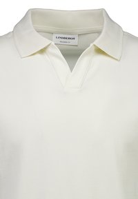 Polo à coupe décontractée en mélange de coton écru, avec un col côtelé et une patte de boutonnage en V. Texture simple et lisse avec un minimum de détails.